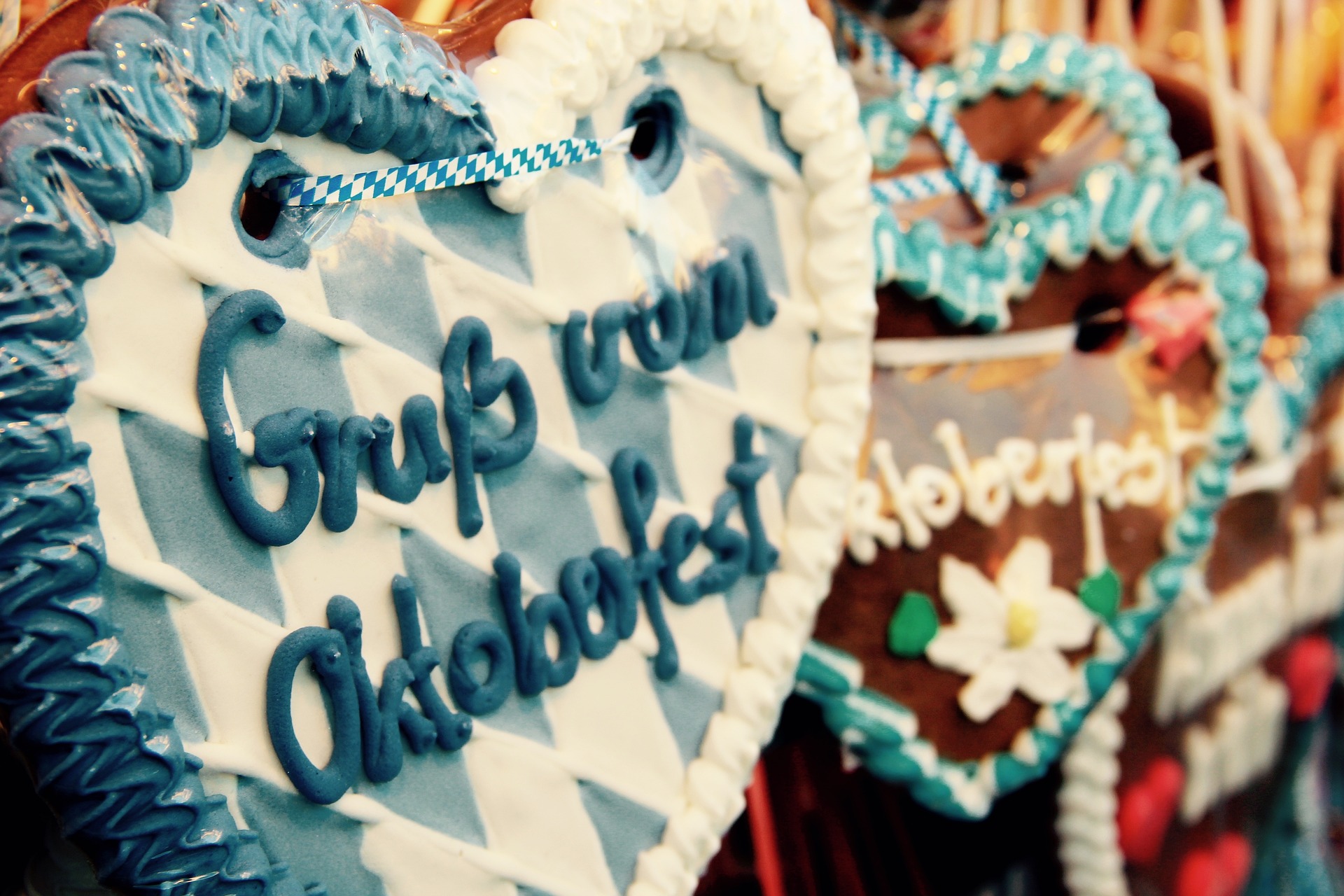 Zwei kunstvoll dekorierte Lebkuchenherzen, eines in Blau-Weiß mit der Aufschrift 'Grüß vom Oktoberfest', das andere in kräftigen Farben mit einer floralen Verzierung.