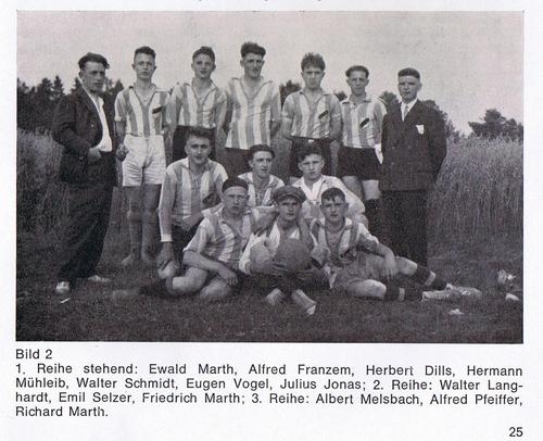 Eine Gruppe von Fußballspielern in gestreiften Trikots posiert auf einem Rasen. Sie stehen und sitzen in zwei Reihen, umgeben von einer ländlichen Kulisse. Einige der Spieler lächeln in die Kamera.